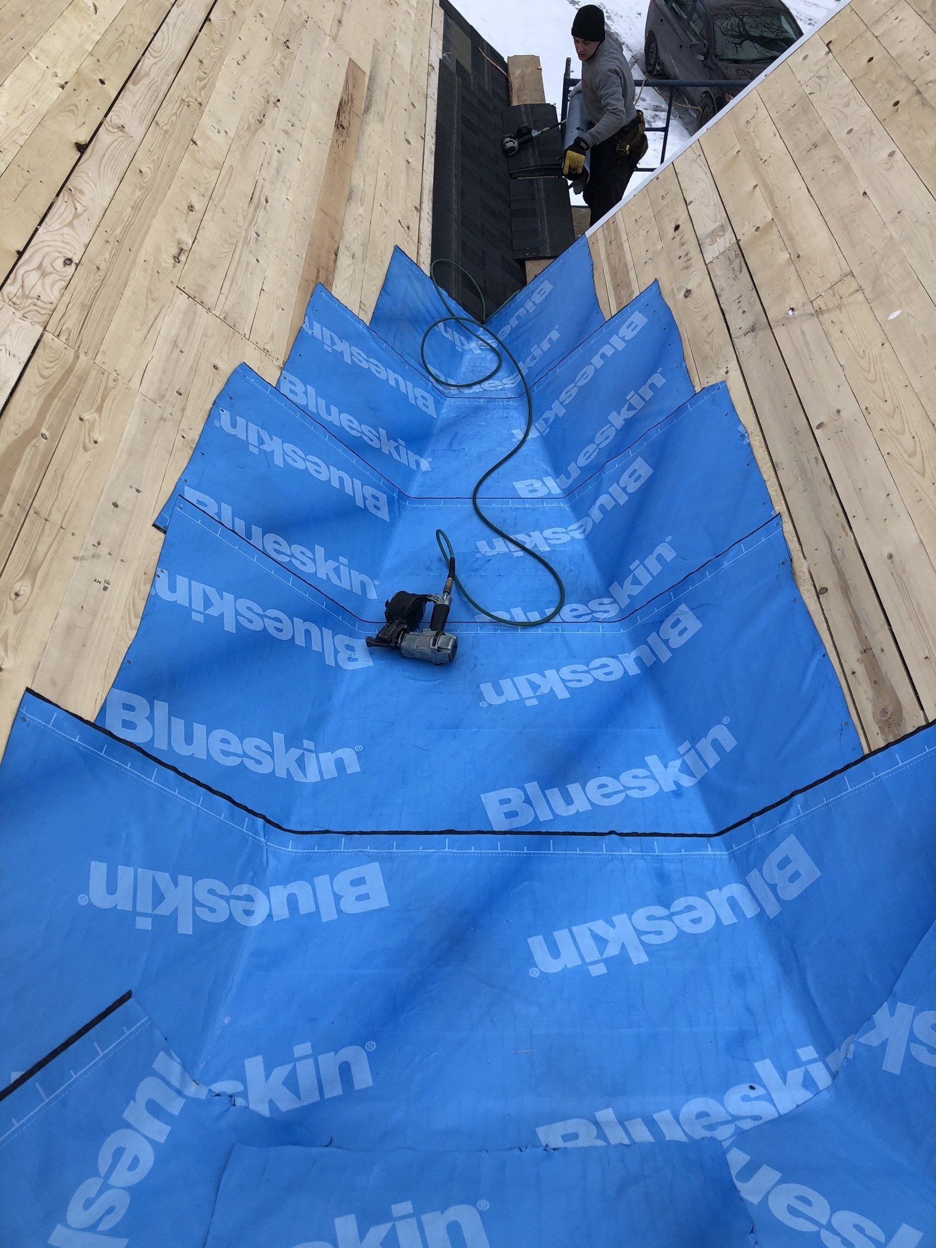 A man is standing on top of a wooden roof with a blue tarp on it.