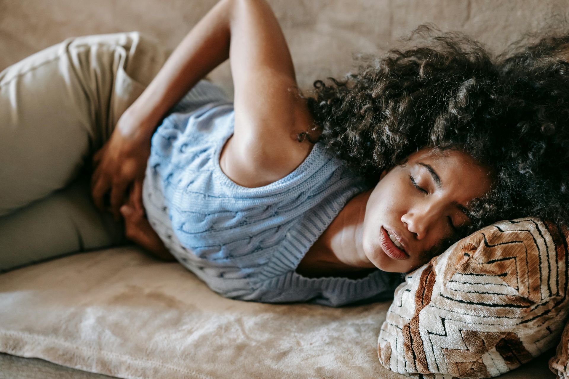 Woman lying on a couch, clutching her stomach, appearing to be in pain.