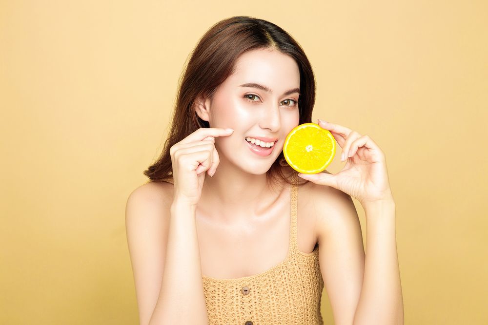 A woman is holding a slice of lemon in front of her face.