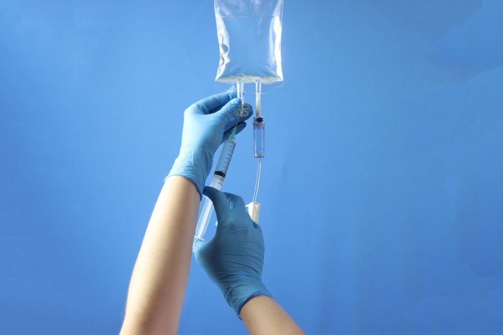 A person wearing blue gloves is holding a syringe and an iv bag.