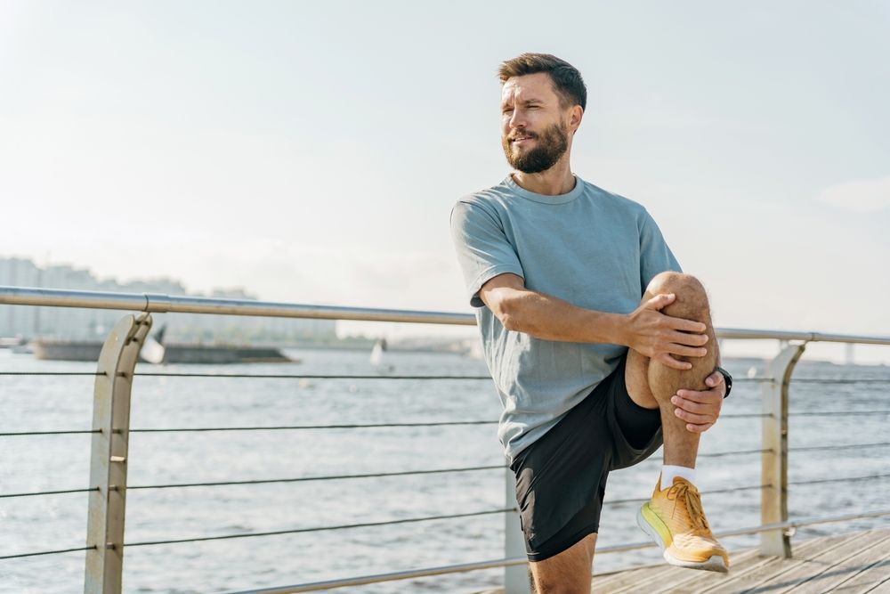 A man is stretching his legs on a pier near the water.