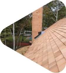 Cedar shake roof under construction with chimney and treeline.