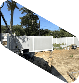 Construction site with trench and white fence in a backyard; wheelbarrow and buckets present.