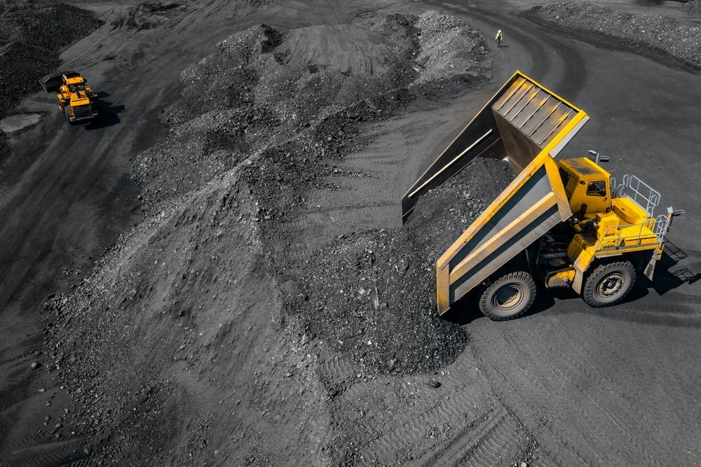 A Yellow Dump Truck is Driving Down a Dirt Road in a Coal Mine — Wilsons Plant In Shellharbour, NSW