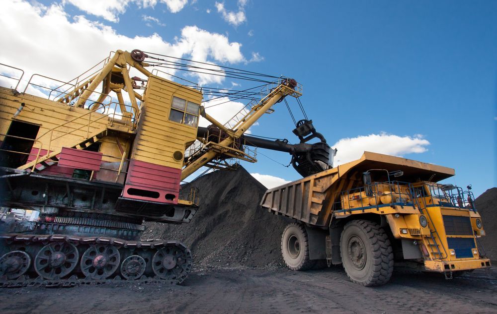 A Large Yellow Dump Truck is Being Loaded With Coal by a Large Excavator — Wilsons Plant In Bellambi, NSW