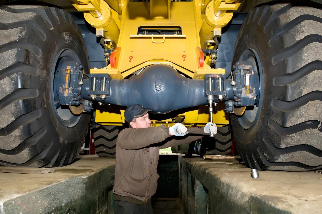 Mechanic Working on the Axle of a Large Yellow Industrial Vehicle, Inside a Shop — Wilsons Plant in Wollongong, NSW