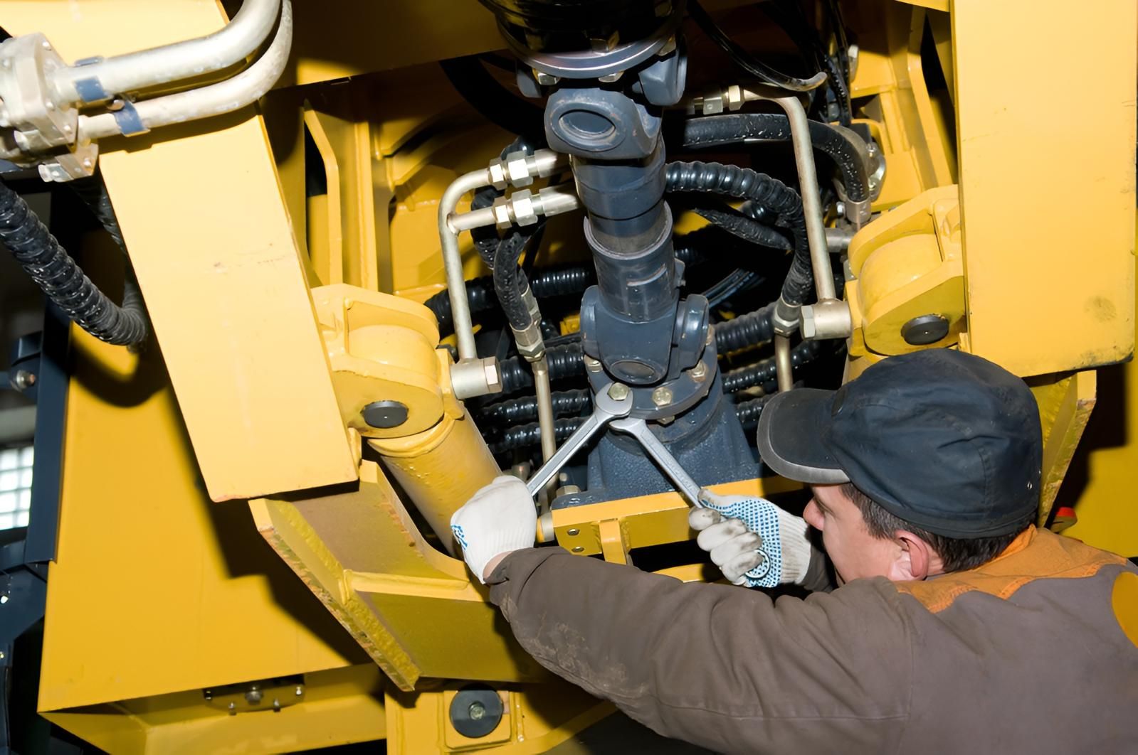 Mechanic in Gloves Using a Wrench on Machinery, With Yellow Equipment Visible, Indoors — Wilsons Plant in Wollongong, NSW
