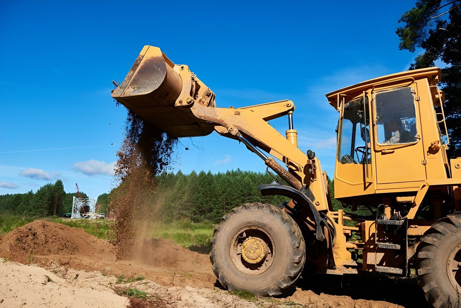 A Yellow Wheel Loader Dumps A Scoop Of Dirt Onto A Pile In A Field