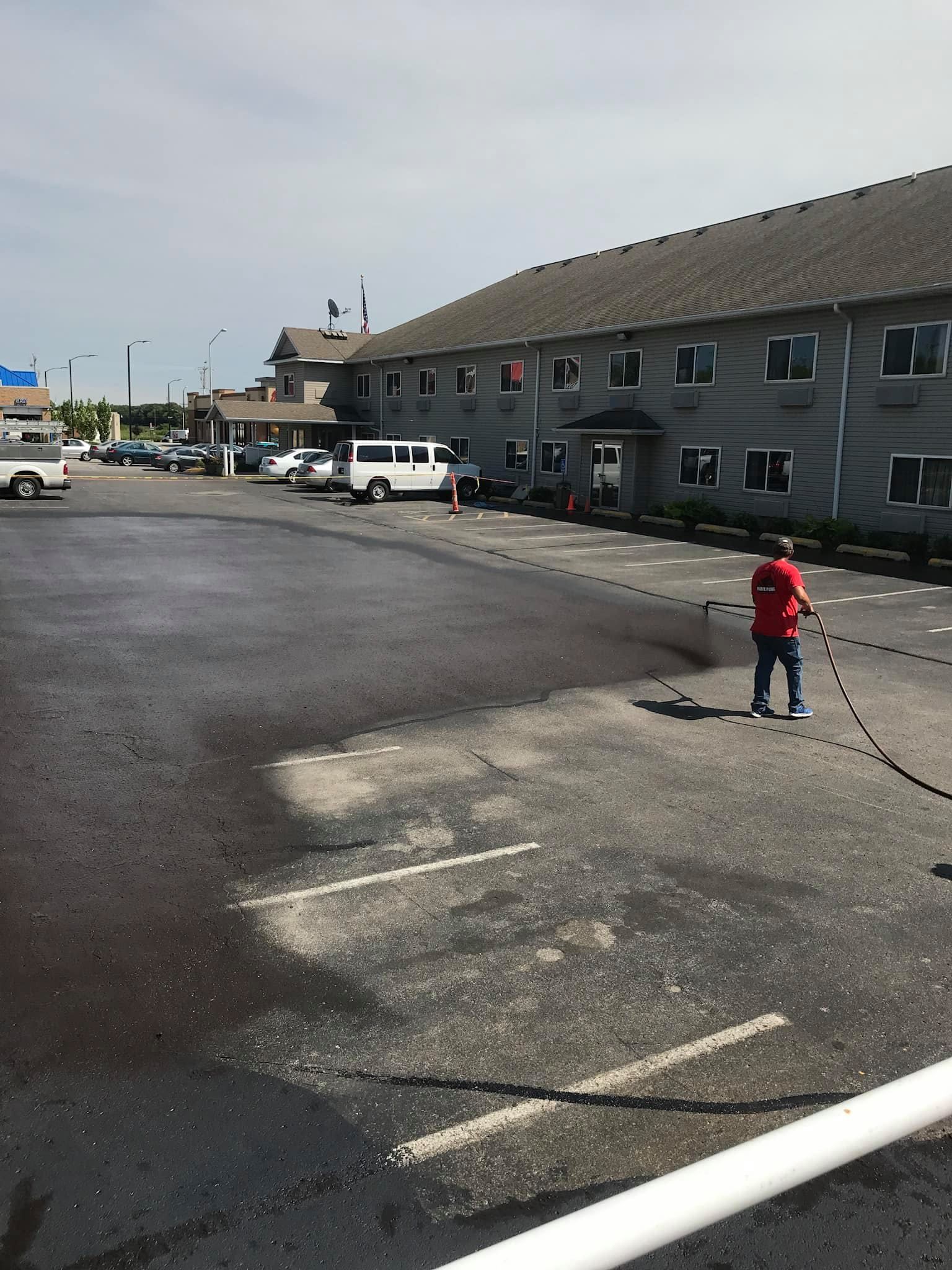 Man applying sealant to a parking lot near a motel.