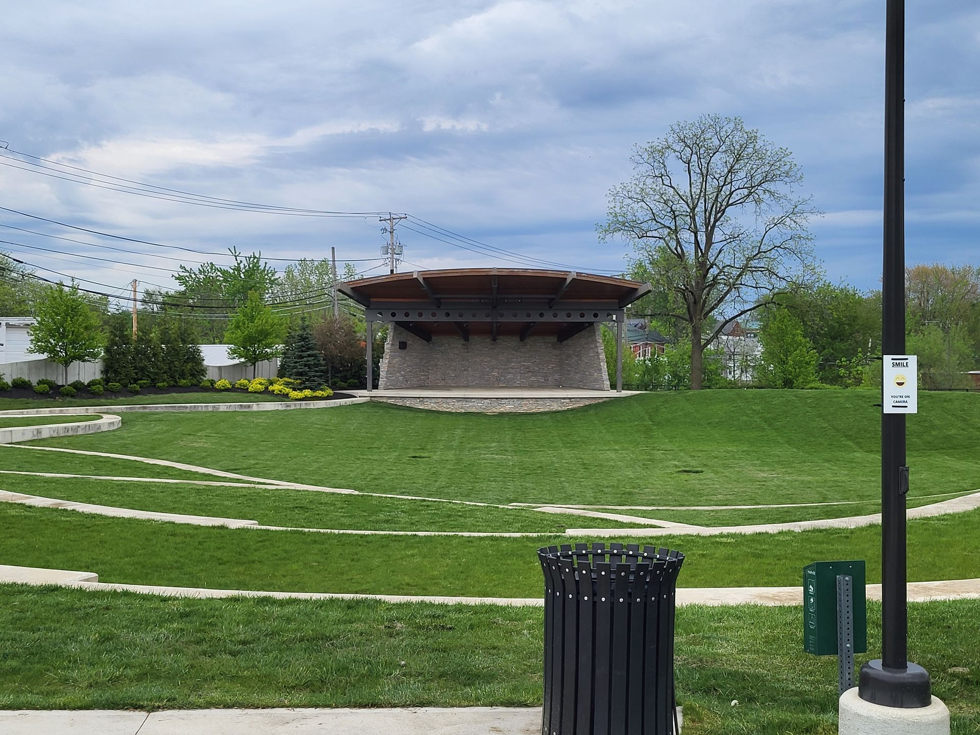 A trash can is sitting in front of a stage in a park.