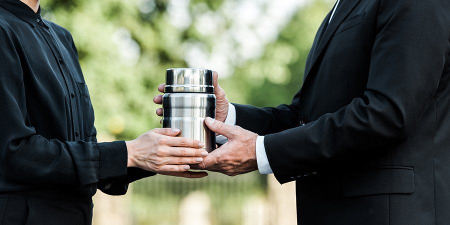 a man in a suit is giving a urn to a woman at a funeral .