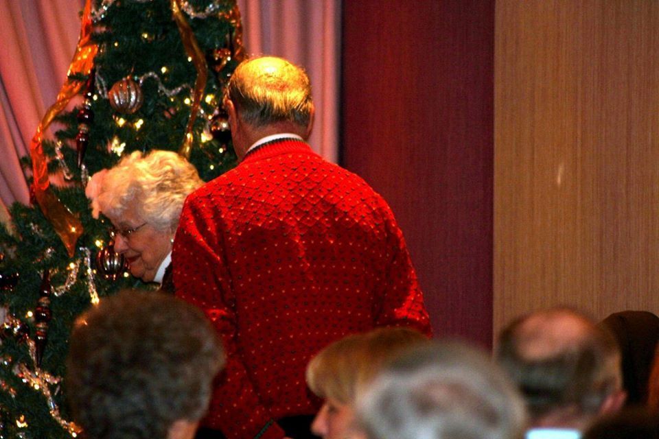 a man in a red sweater stands in front of a christmas tree