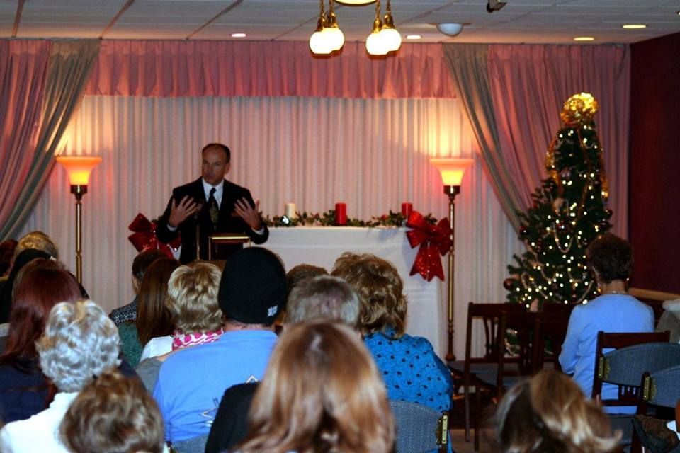 a man is giving a speech to a group of people in front of a christmas tree