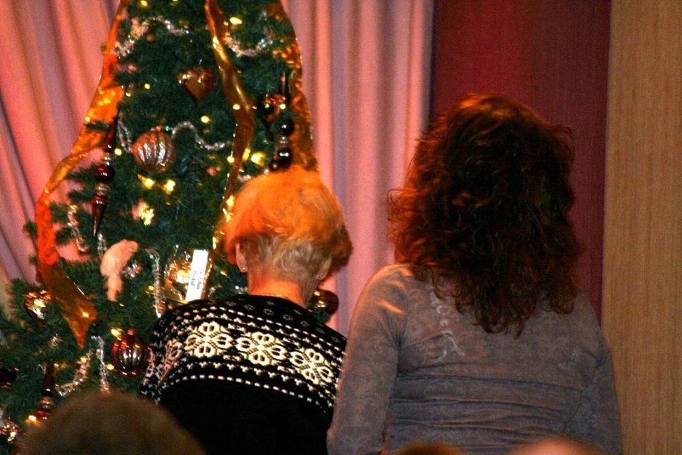 two women are sitting in front of a christmas tree