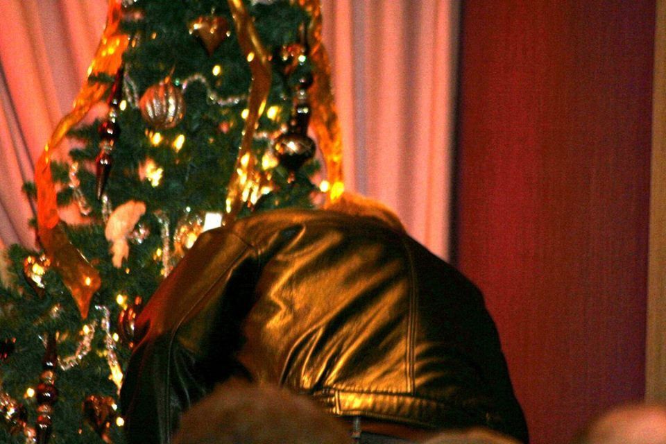 a man in a leather jacket is standing in front of a christmas tree