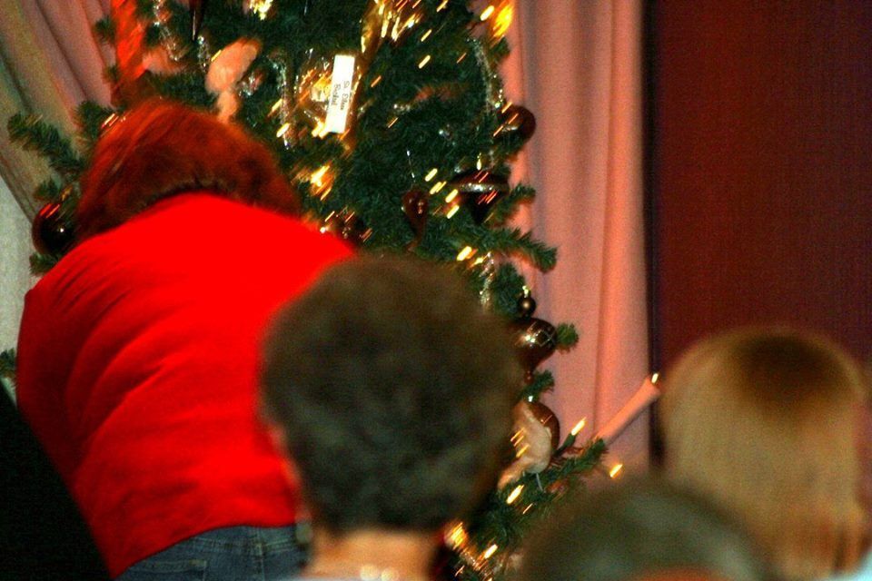 a woman in a red sweater is decorating a christmas tree