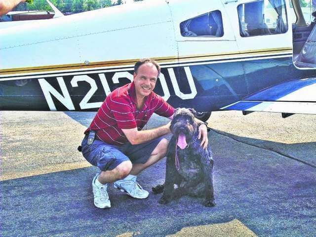 a man kneeling down with a dog in front of a plane with the number n215u on it