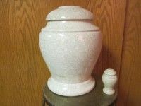 a white urn is sitting on top of a wooden table next to a smaller urn .
