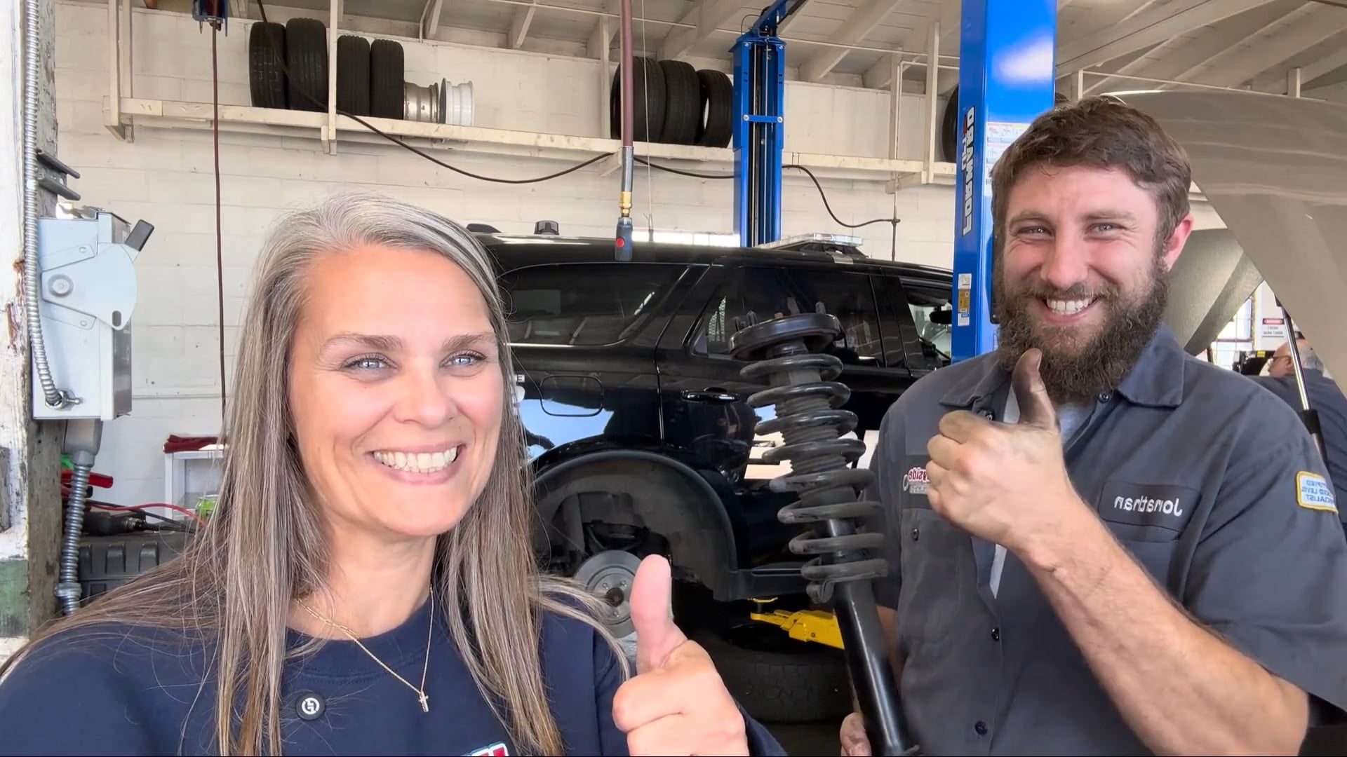 Wayside Garage team members smiling in the shop, holding a strut 