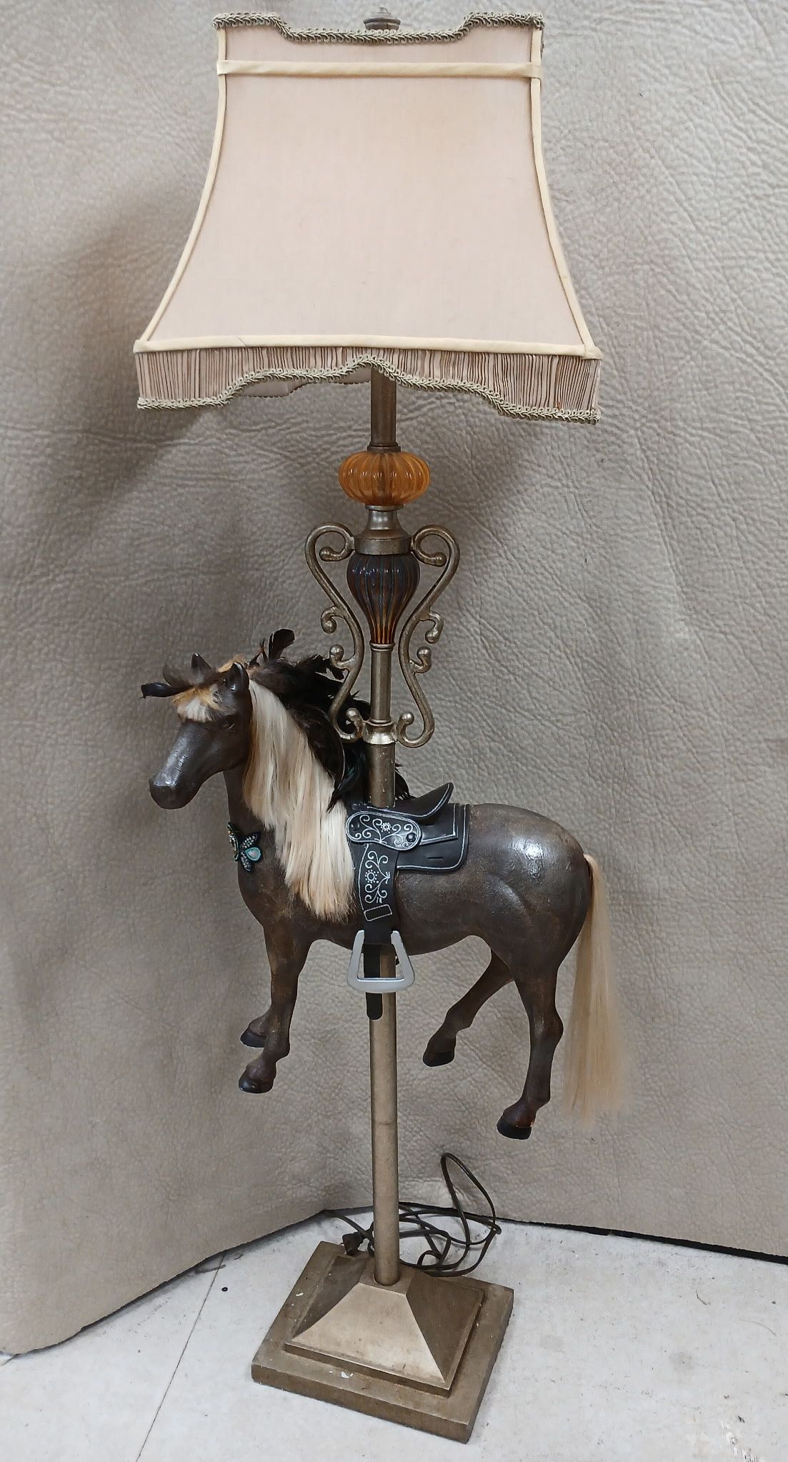A decorative floor lamp with a horse figurine, beige lampshade, and ornate gold details.