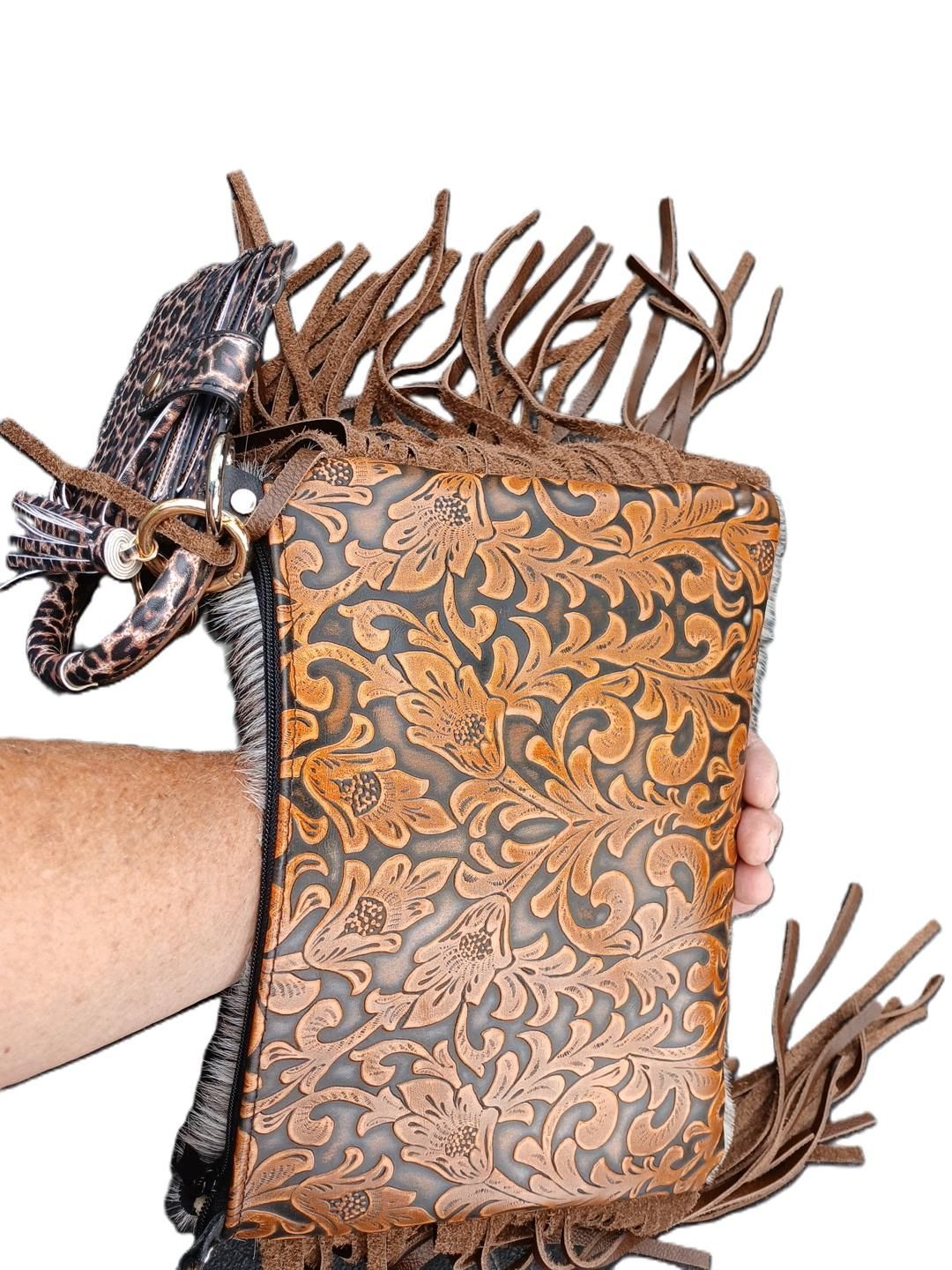 Hand holding a brown leather purse with embossed floral design and fringe.
