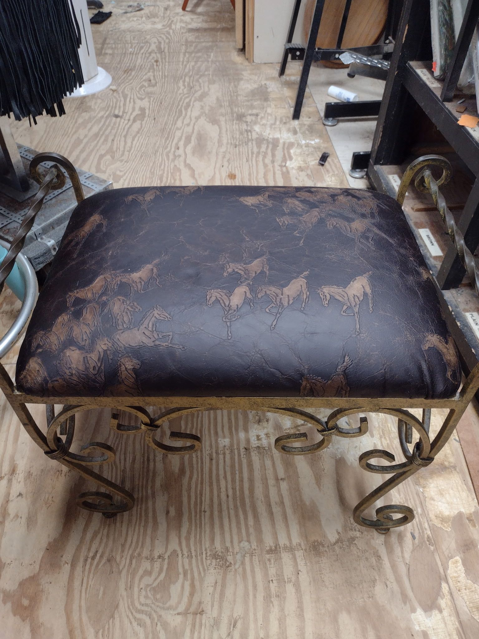 Ornate metal vanity stool with dark brown, horse-patterned cushion; set on a wood floor.