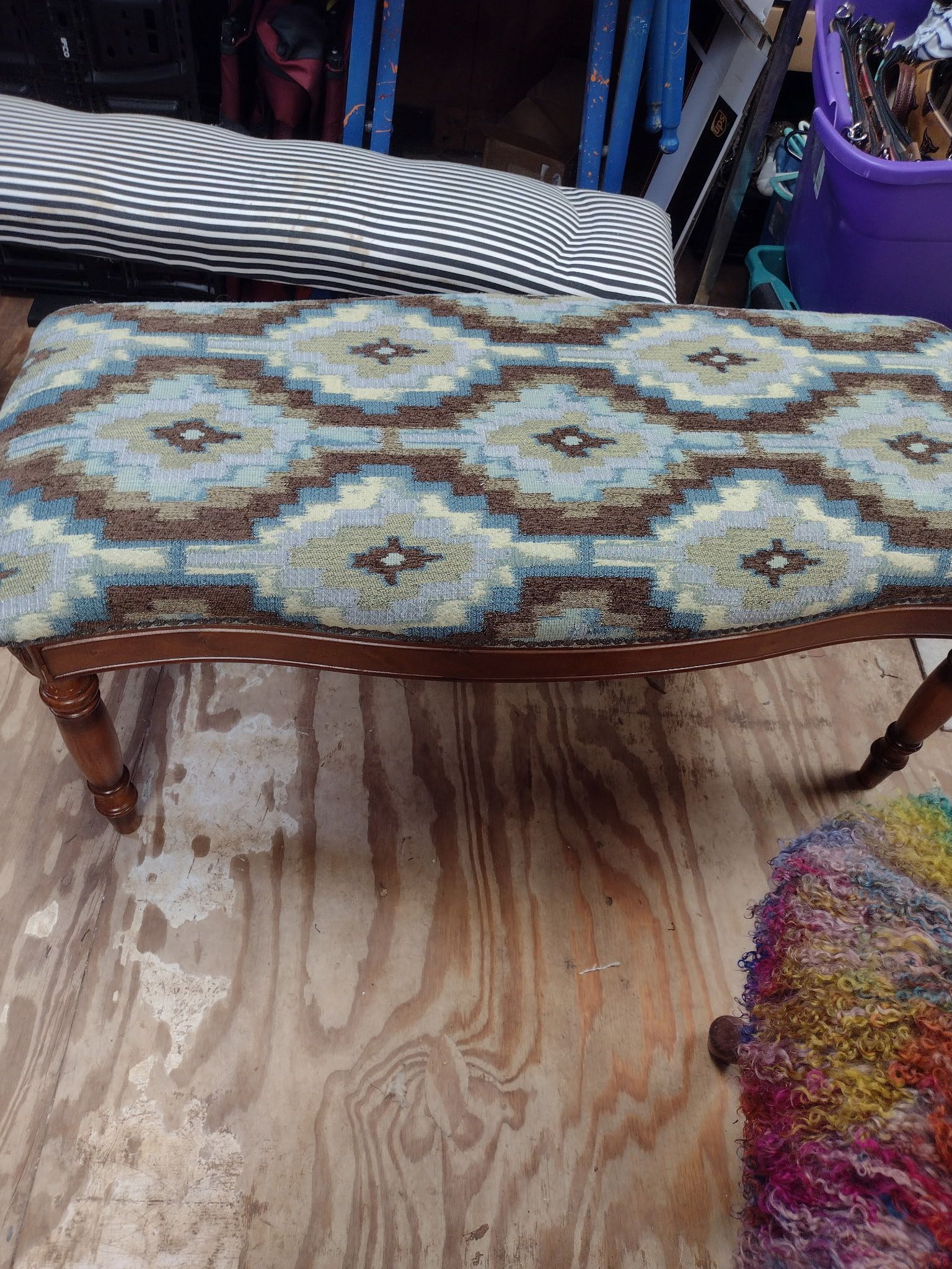 Upholstered bench with blue and brown geometric pattern, wooden legs, and decorative tacks. Sits on a wooden floor.