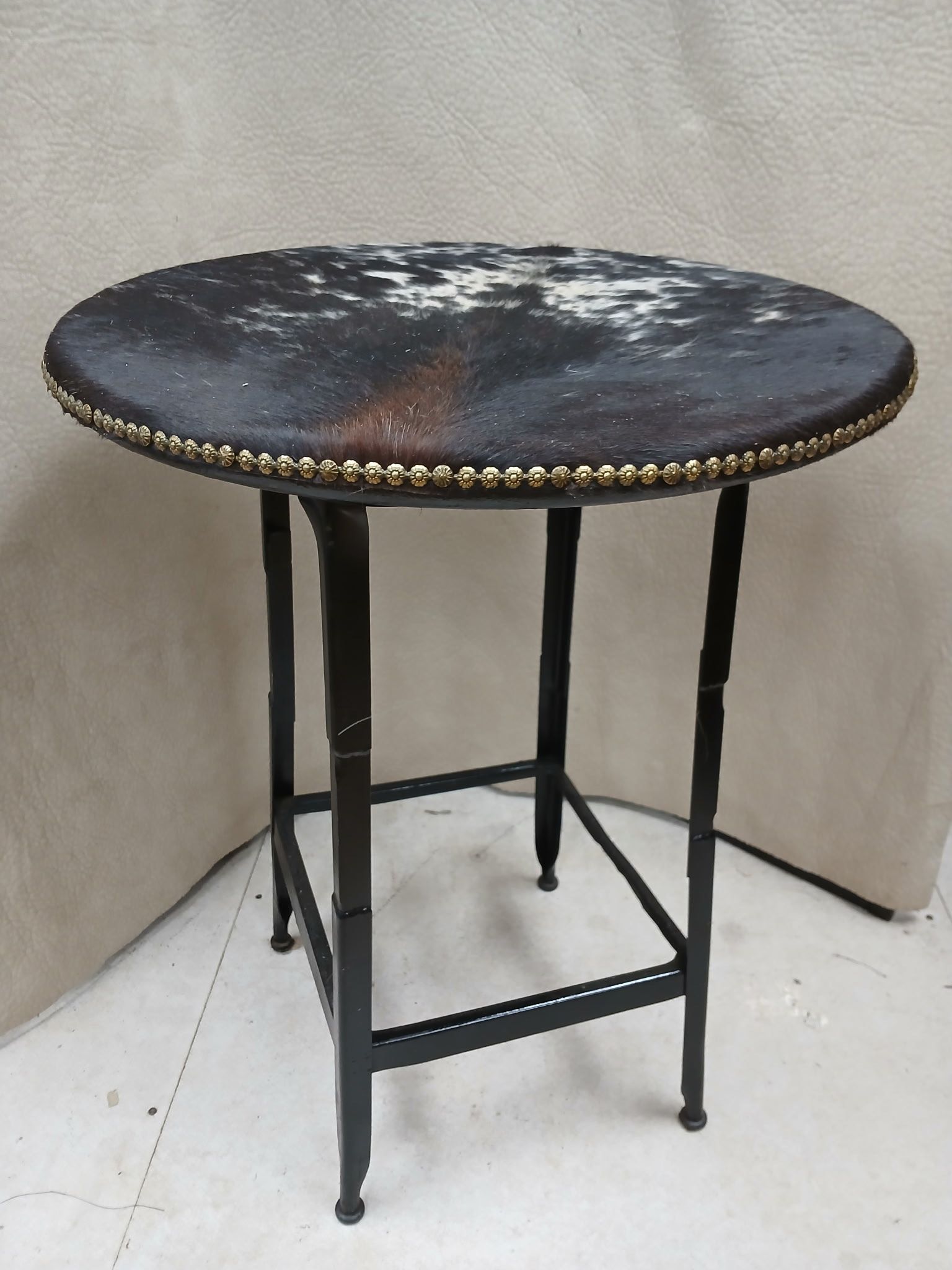Round side table with a cowhide top, dark metal frame, and studded trim.