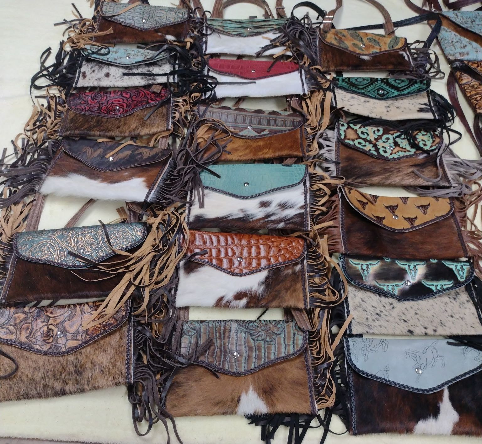 Pile of handcrafted leather purses with cowhide and fringe details, in various colors and styles.