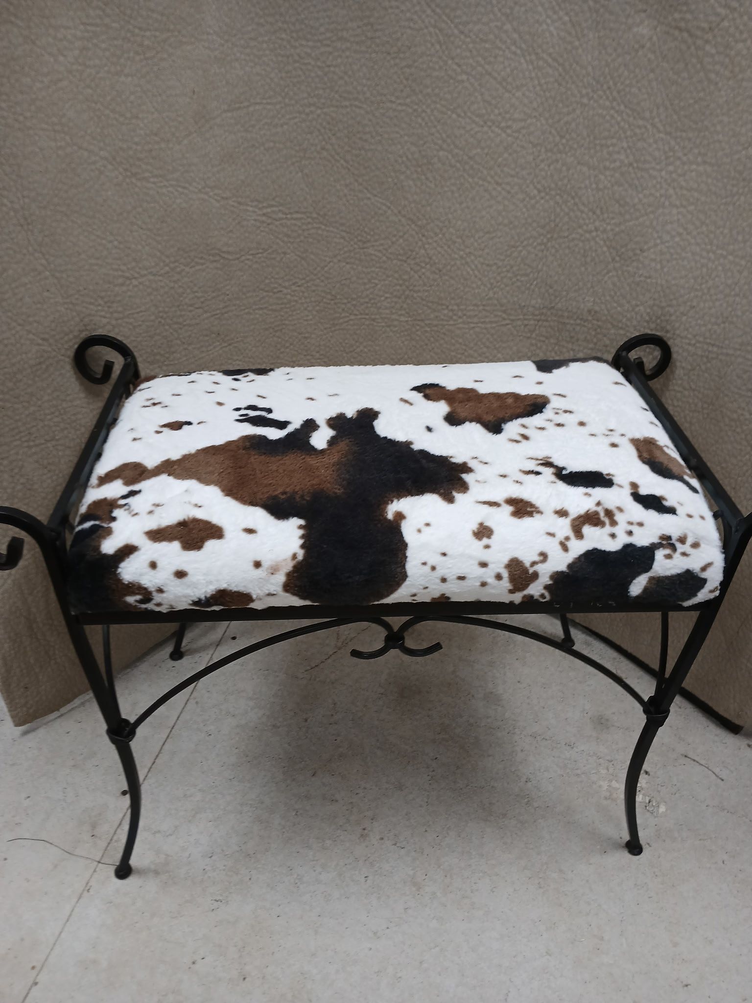 Cowhide upholstered bench with a black wrought iron frame.