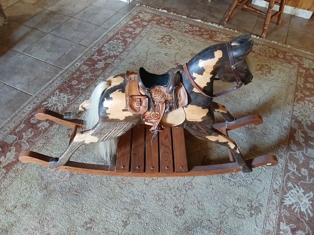 Wooden rocking horse with brown and tan paint, on a patterned rug.