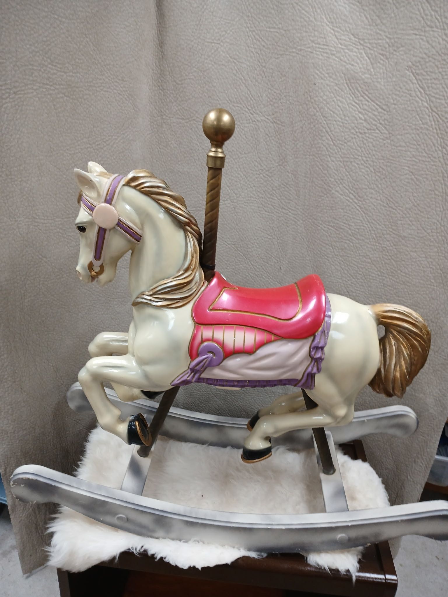 A white rocking horse with a red saddle is sitting on a wooden table.
