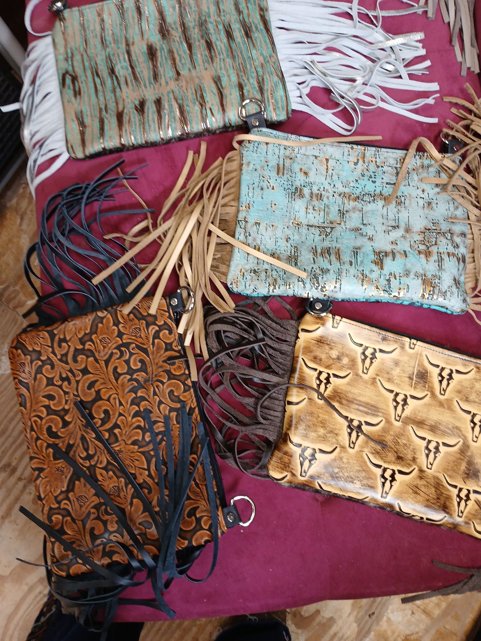 Five leather clutch purses with fringe; turquoise, brown, and patterned with floral and steer head designs.