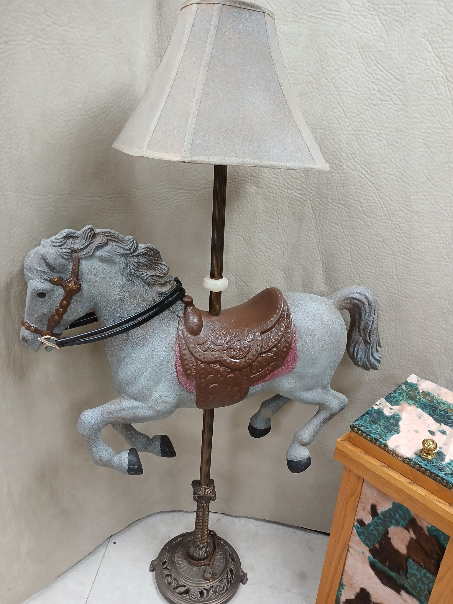 A decorative lamp featuring a grey carousel horse with a brown saddle and a light-colored lampshade.