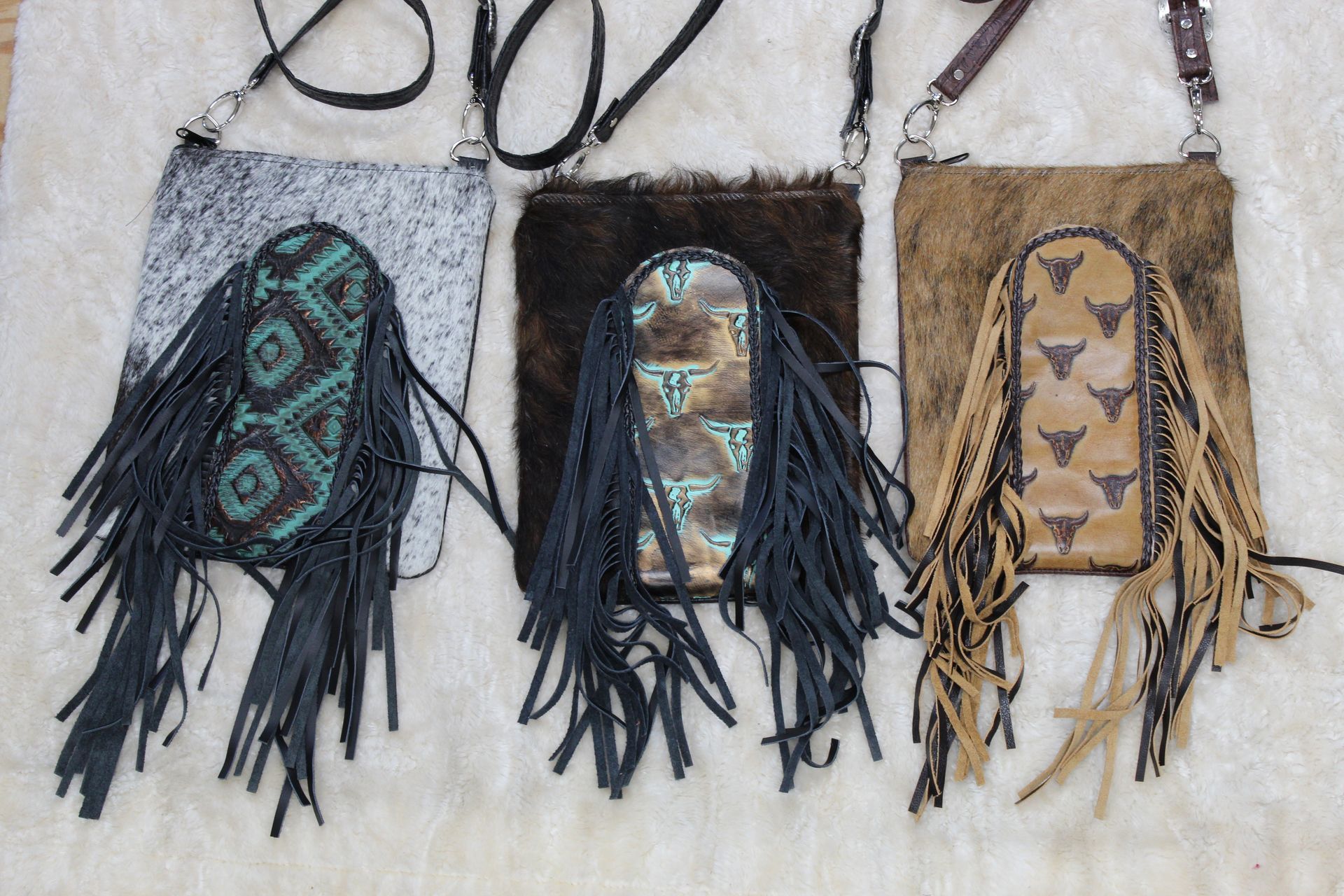 Three fringed leather crossbody bags: silver, brown, and tan, with decorative turquoise, brown, and tan fronts with steer head patterns.