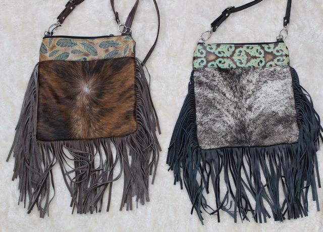 Two fringed, leather crossbody bags with cowhide fronts. One bag is brown and the other is black.