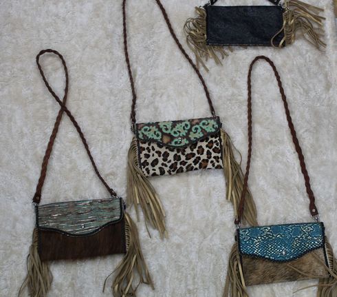 Four small, fringed leather crossbody bags in various animal prints and colors sit on a light-colored surface.