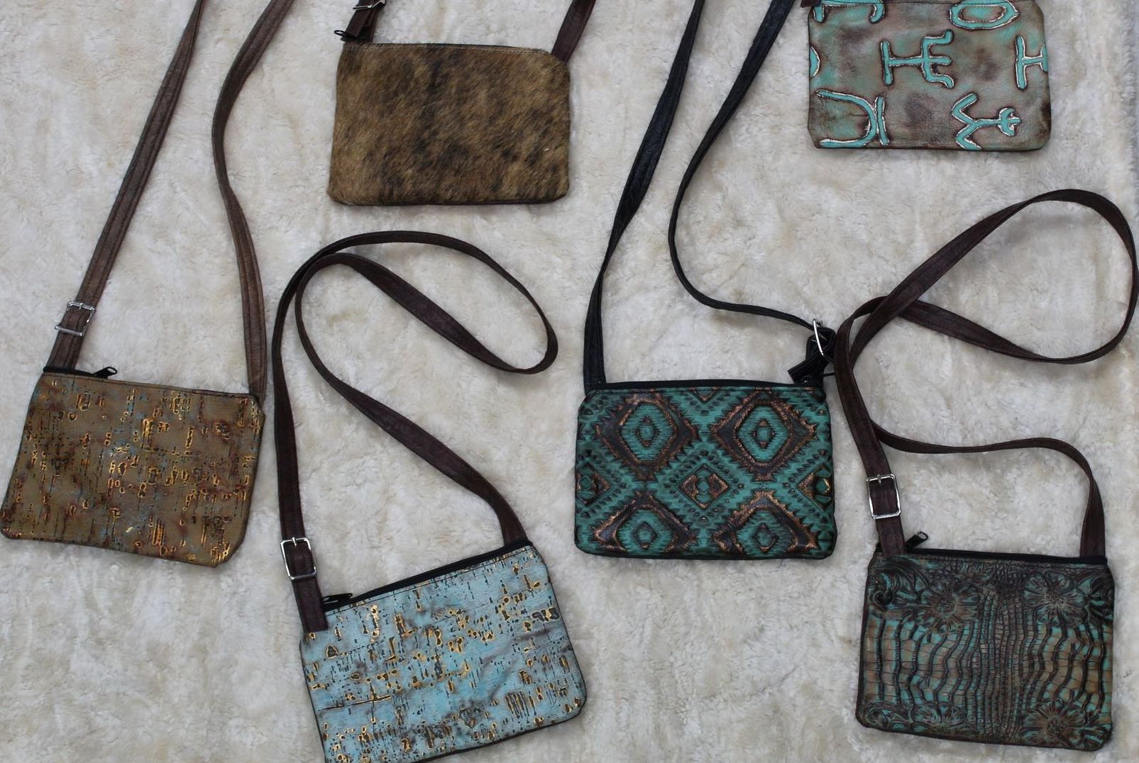 Assortment of small, rectangular cross-body bags in various textures and patterns, including brown, turquoise, and embellished designs, lying on a light-colored surface.