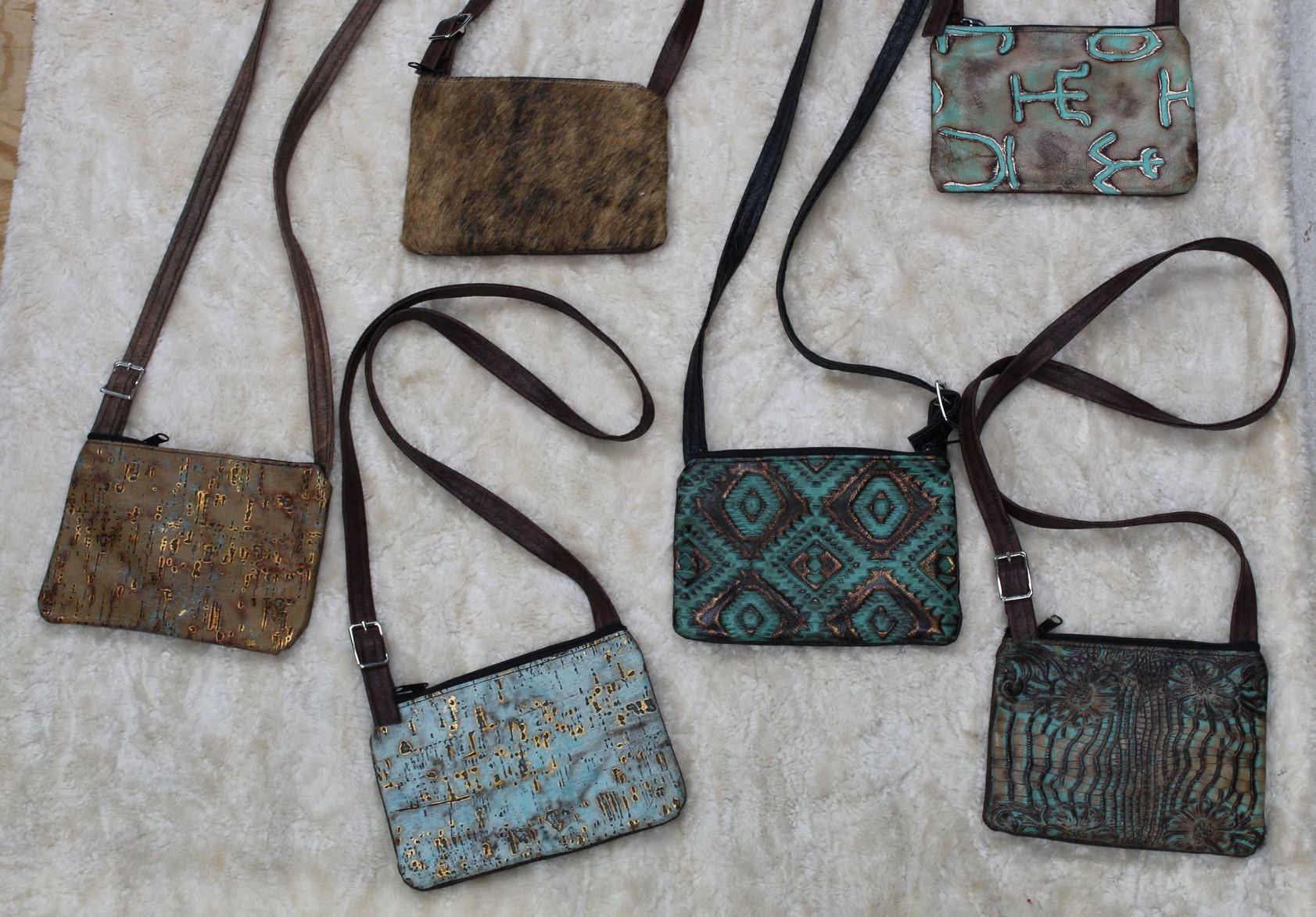 Six small crossbody bags with brown straps, each with a different textured or patterned front in shades of brown, teal, and blue.