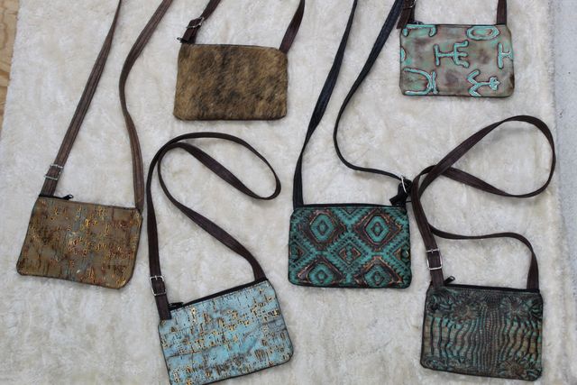 Six small, rectangular crossbody bags with brown straps on a light-colored surface. The bags are textured and in various colors like brown, teal, and gold.