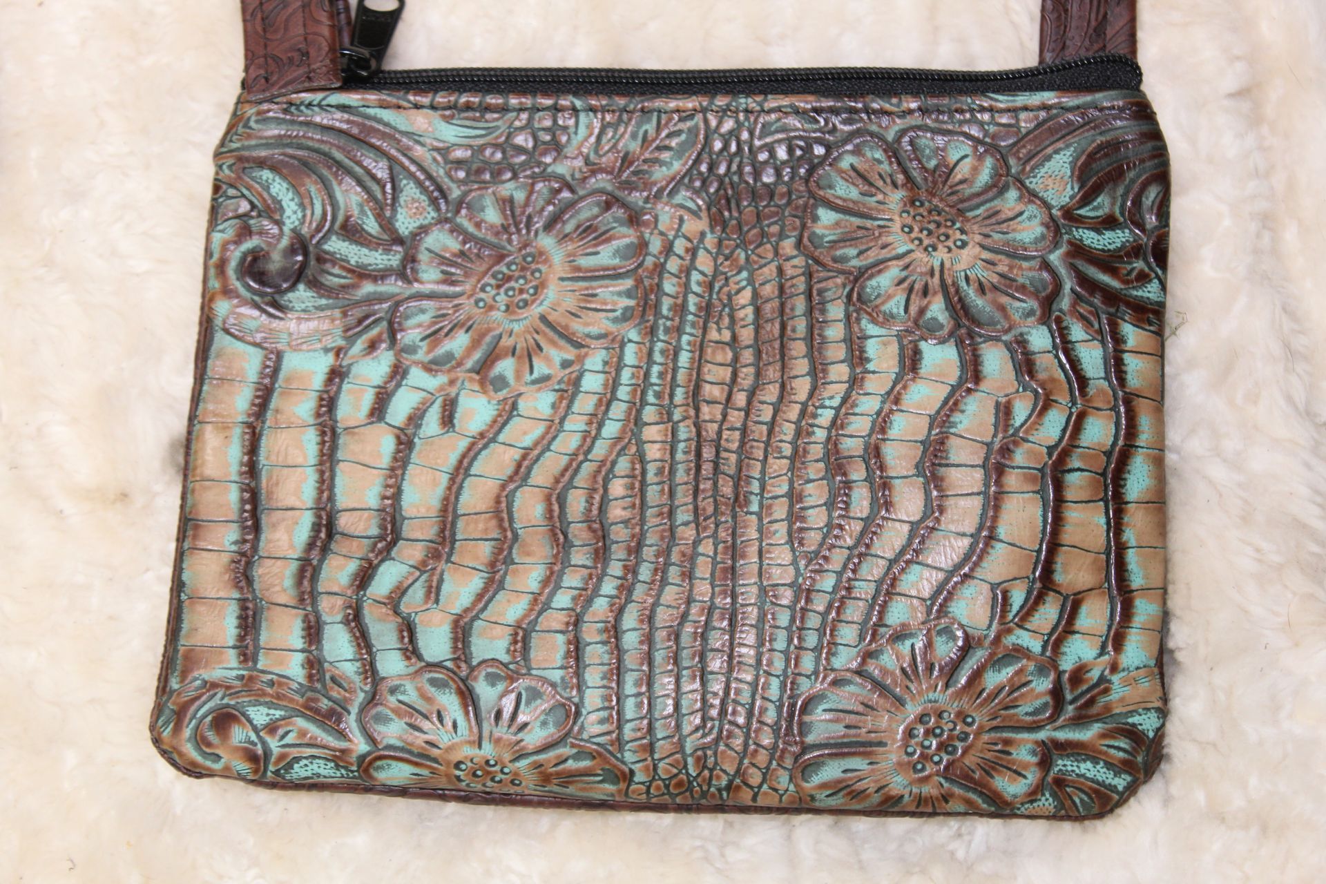 Turquoise and brown leather crossbody bag with floral and vertical line embossed design.