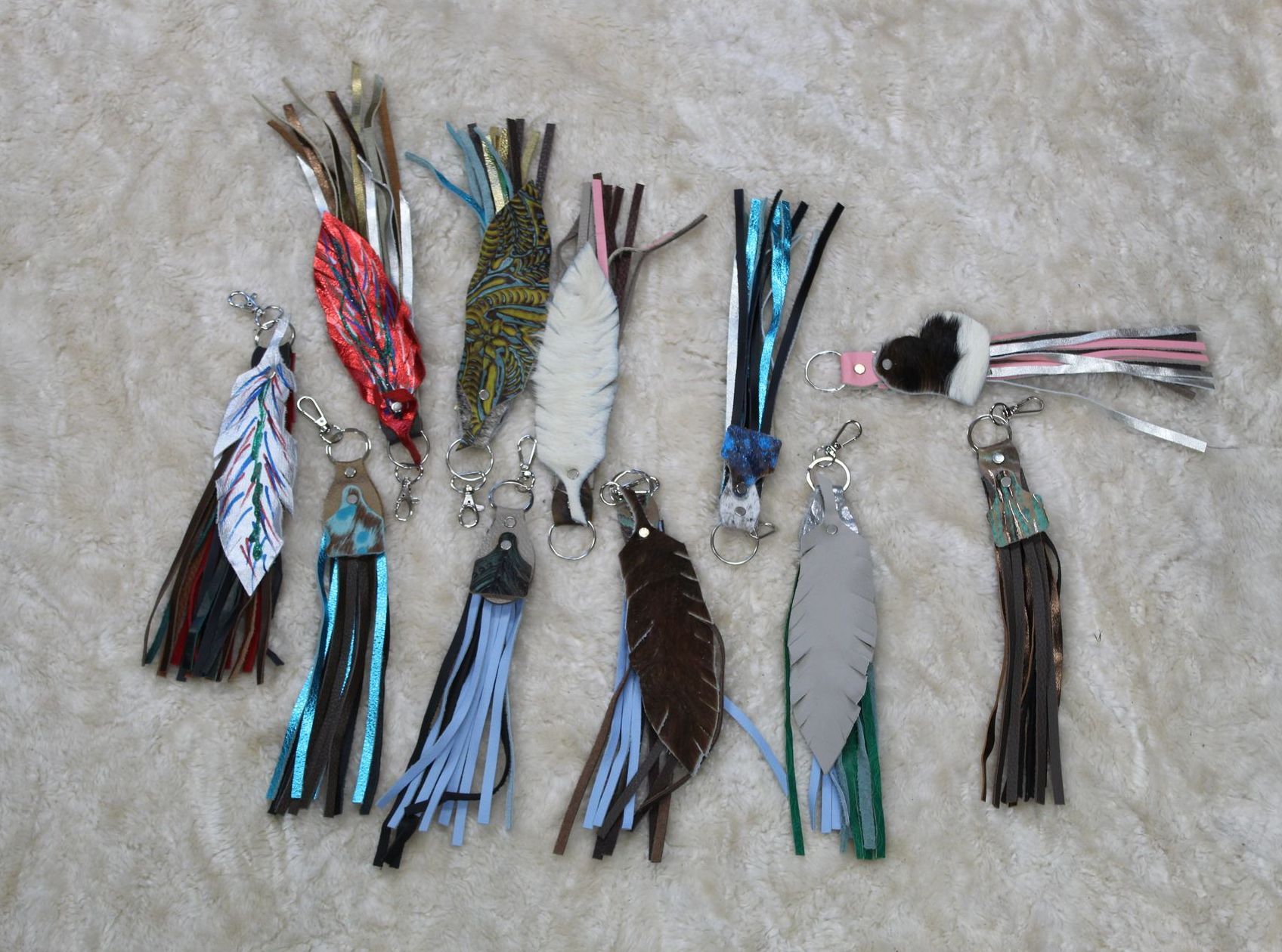 Collection of colorful handmade keychains with leather and fringed details, spread on a light textured surface.