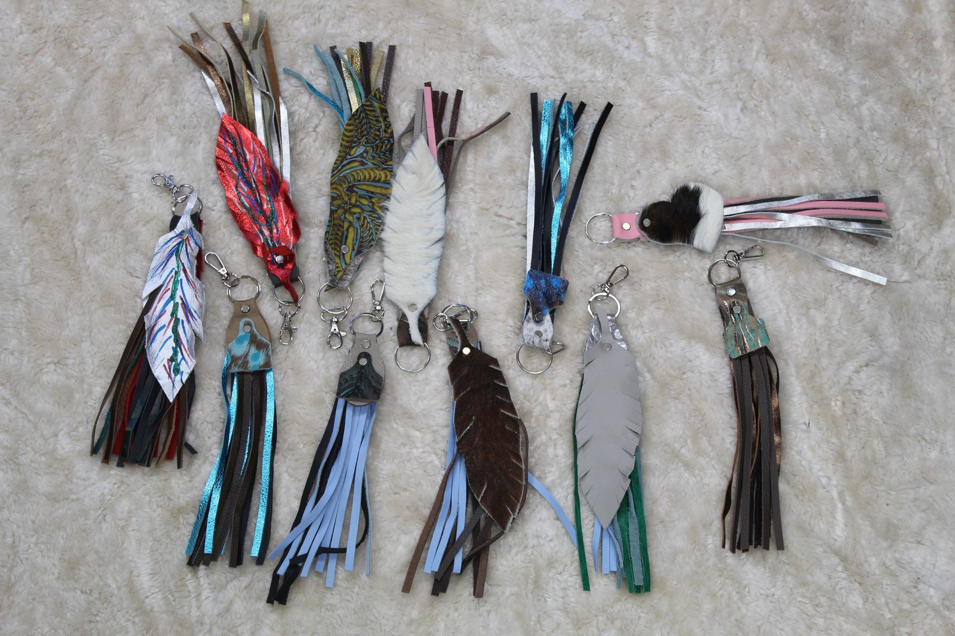 A collection of colorful leather tassel keychains displayed on a neutral-colored surface.