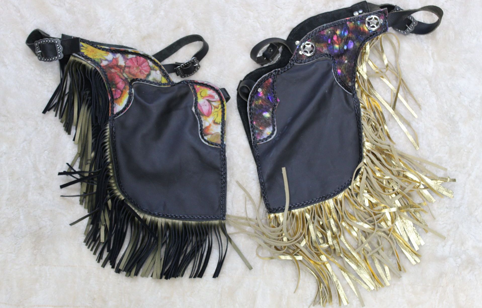 Pair of black chaps with decorative floral patterns on the upper portion and long fringe. The fringe colors are black and gold.