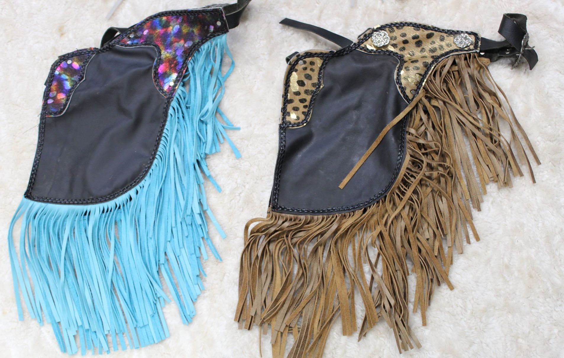 Two pairs of colorful chaps with fringe. One is blue and black, the other brown and leopard print.