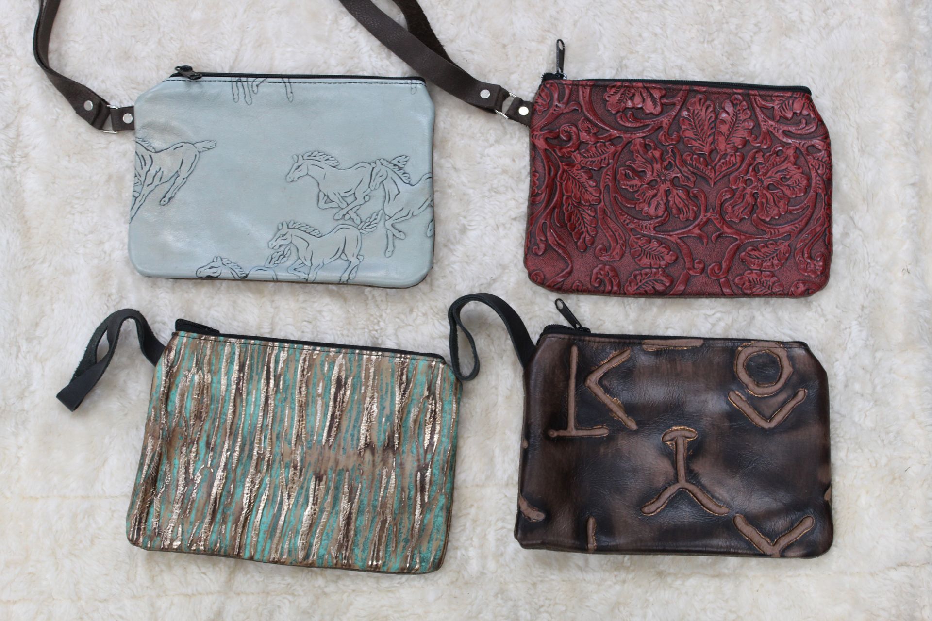 Four leather crossbody bags in various colors and textures: blue with horse outline, burgundy floral pattern, turquoise stripe, and brown with abstract design.