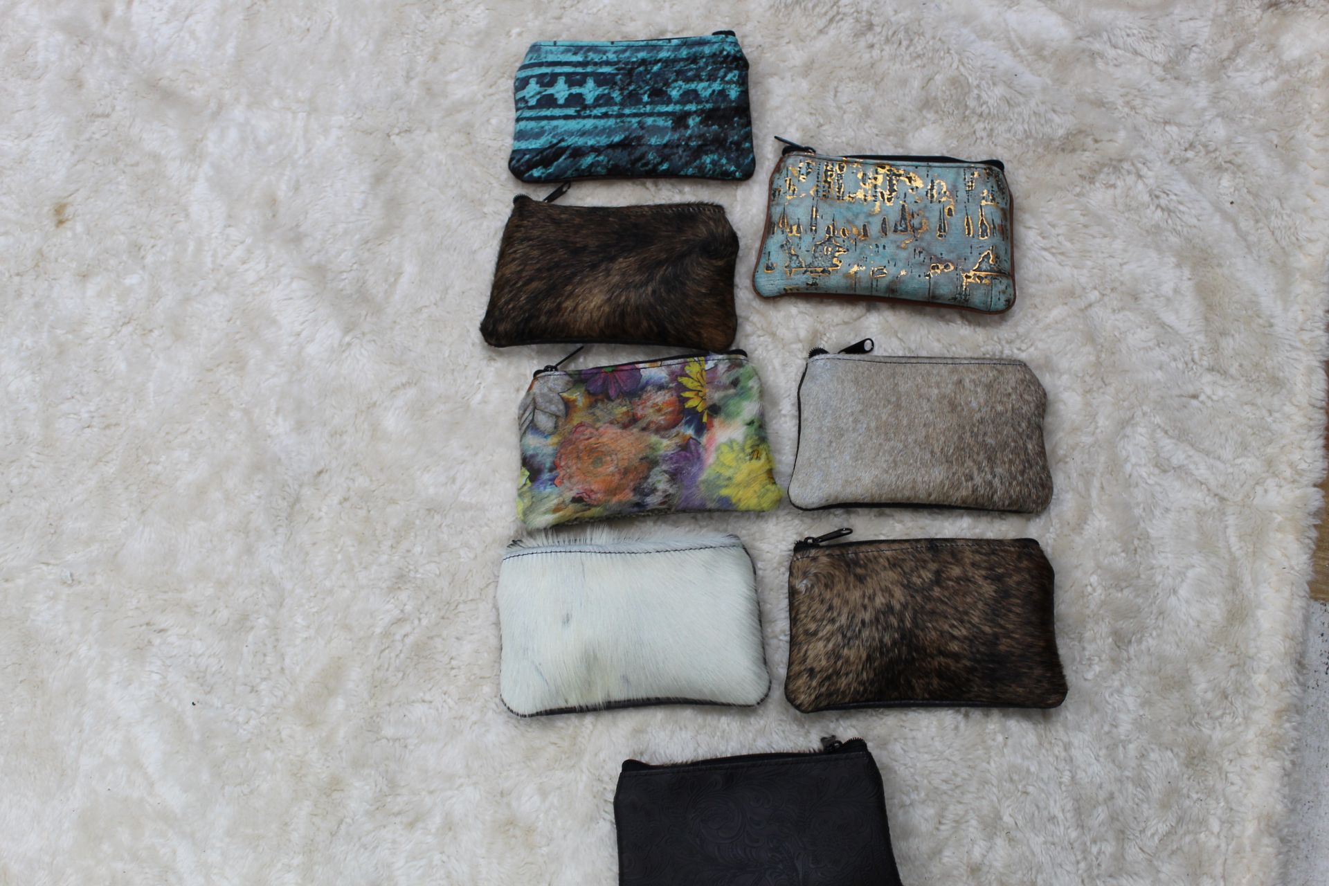 Nine small zippered pouches of various colors and textures, arranged on a white fluffy surface.