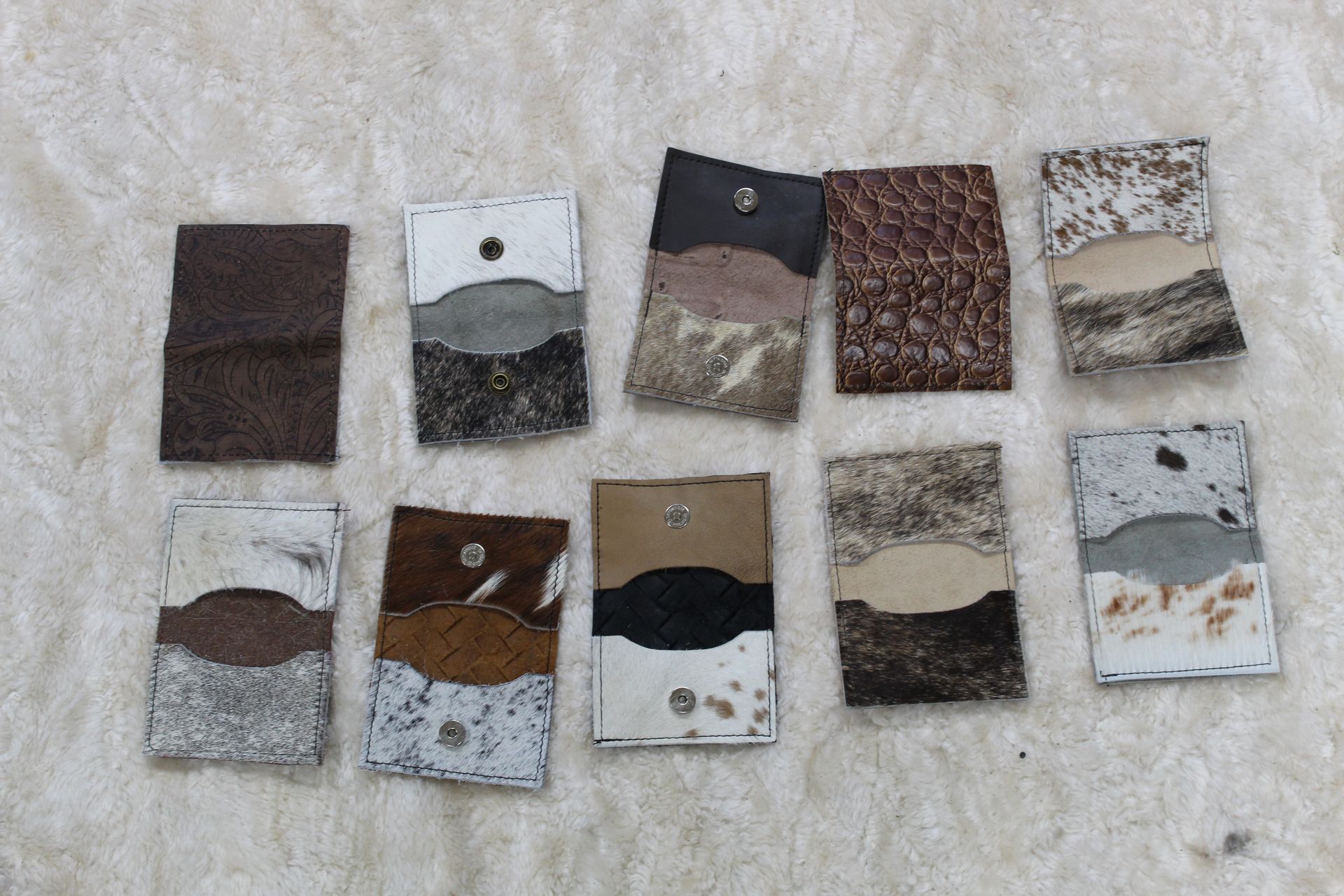 Ten handcrafted leather cardholders of various designs and colors are displayed on a beige surface.