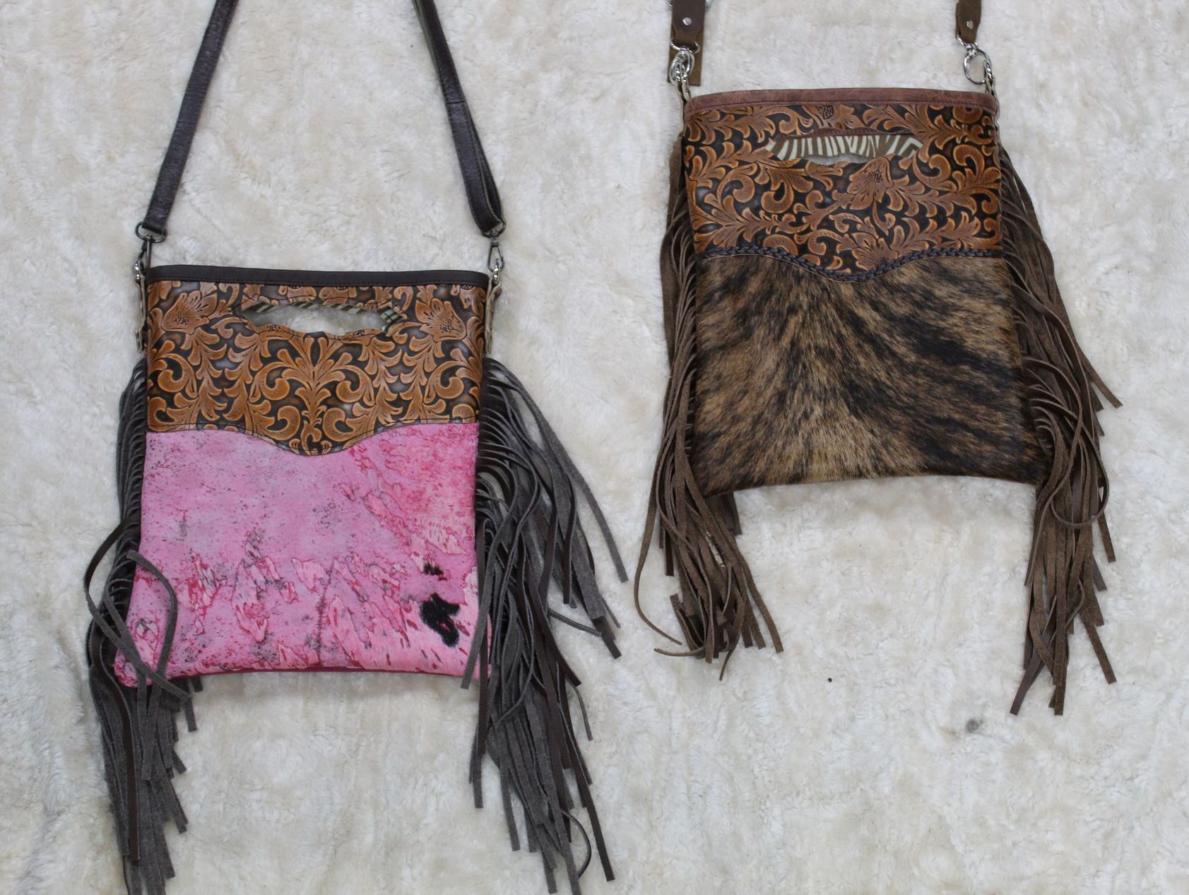 Two leather crossbody bags with fringe. One is pink, the other is brown with a cowhide pattern. Both have long brown straps.