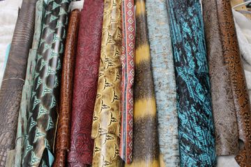 Close-up of a collection of various patterned leather hides in shades of brown, teal, and red, likely for crafting.